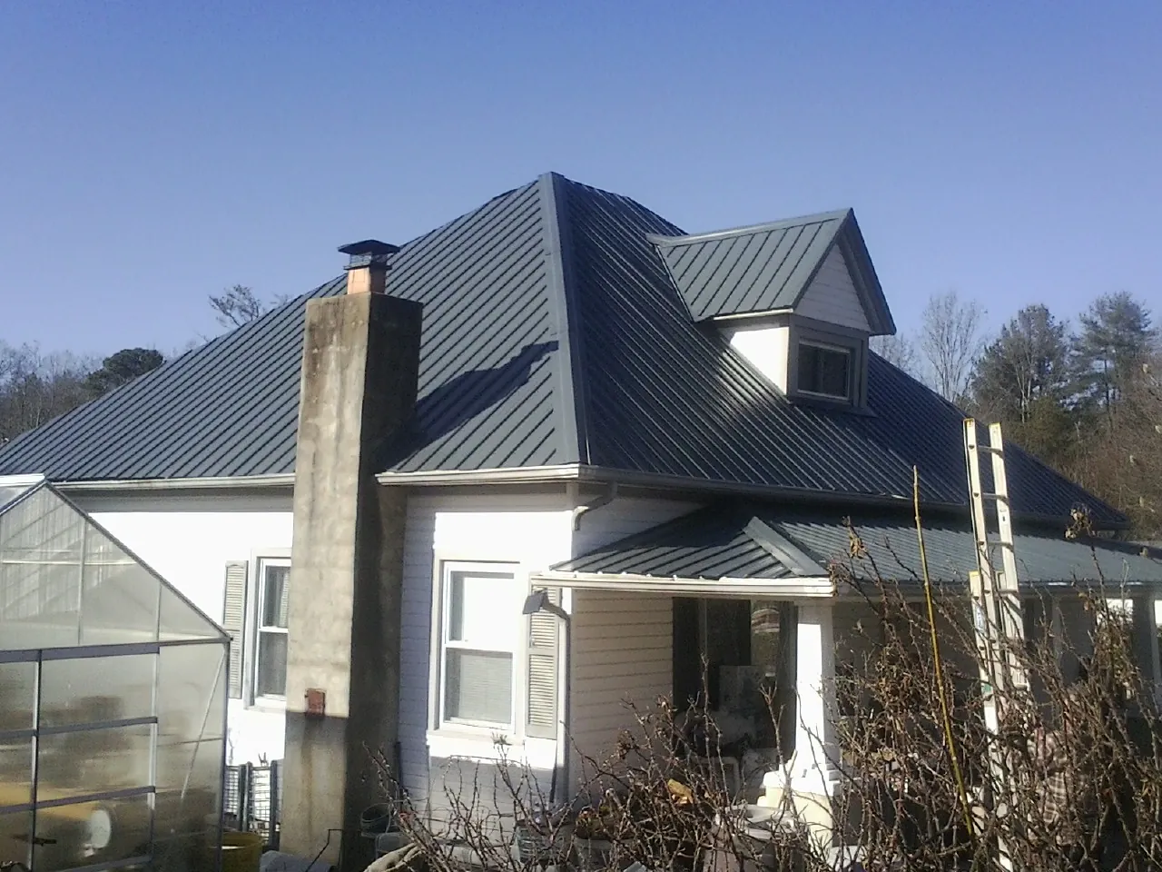 Dark blue standing seam metal roof on a white farmhouse with dormer — Slate & Tile Roof Repair by Roofing Brothers in Upsala