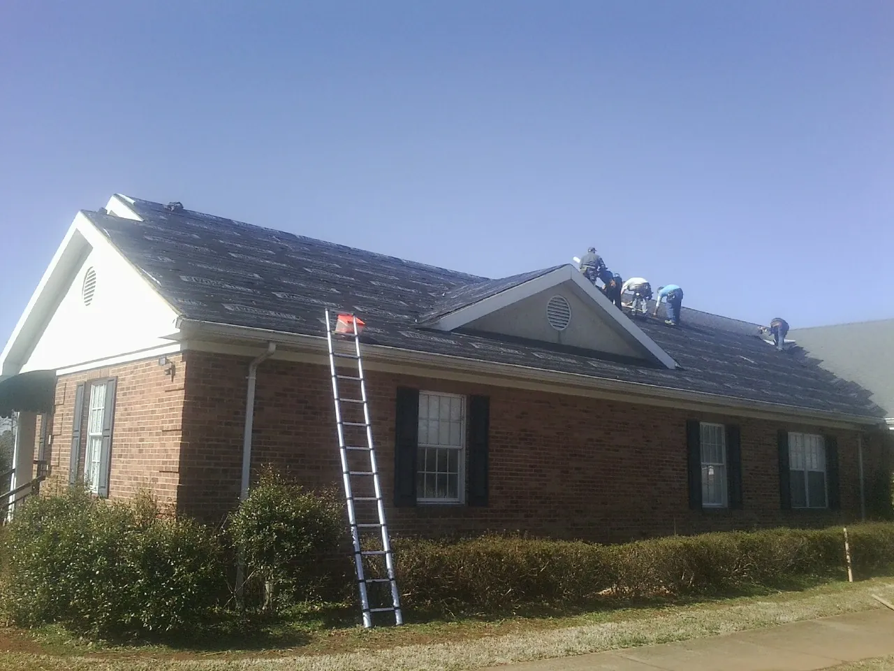Crew tearing shingles off a brick ranch roof with a ladder set — Emergency Roof Repair work by our crew in Upsala