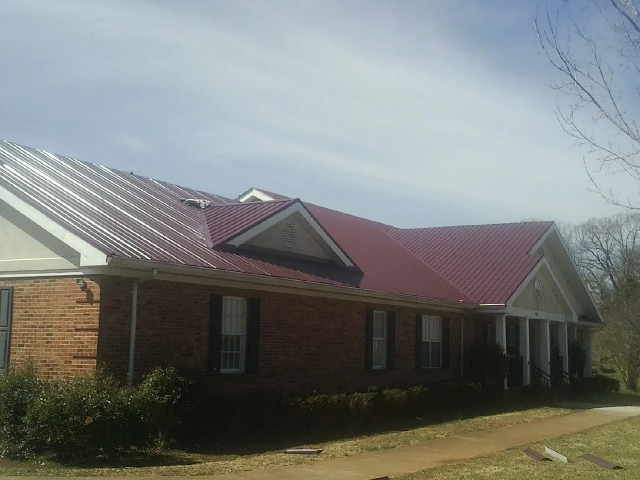 Red metal roof with gabled entries on a long brick building, from a Hail Damage Roof Repair job in Upsala