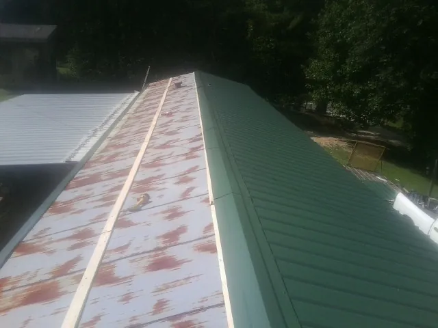 Old rusted panels beside newly installed green metal roofing — Wind Damage Roof Repair by Roofing Brothers in Upsala