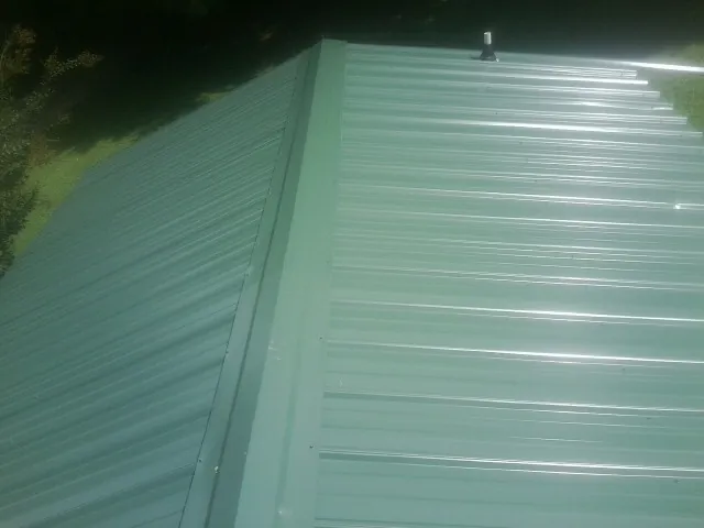New green metal panels meeting at the ridge of a roof — Flat Roof Repair work by our crew in Upsala
