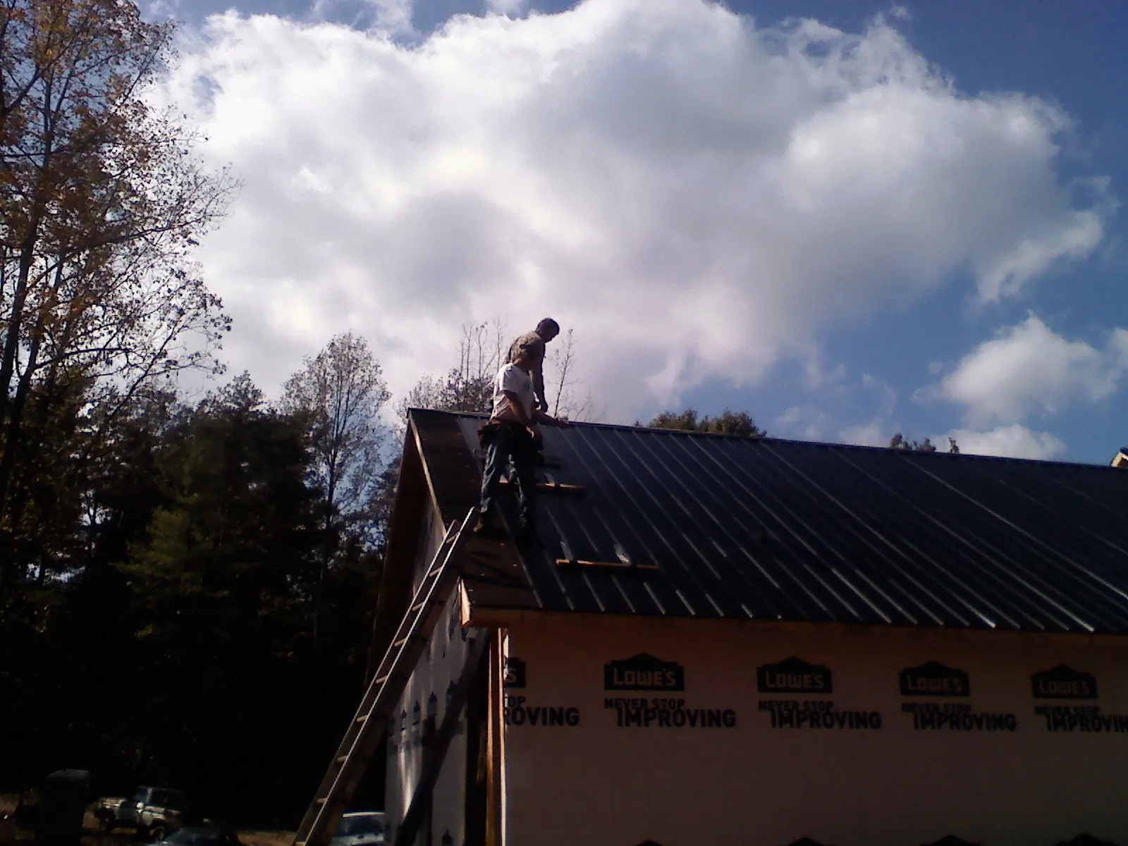 Roofer fastening dark metal panels high against a cloudy sky, from a Roof Inspection job in Upsala