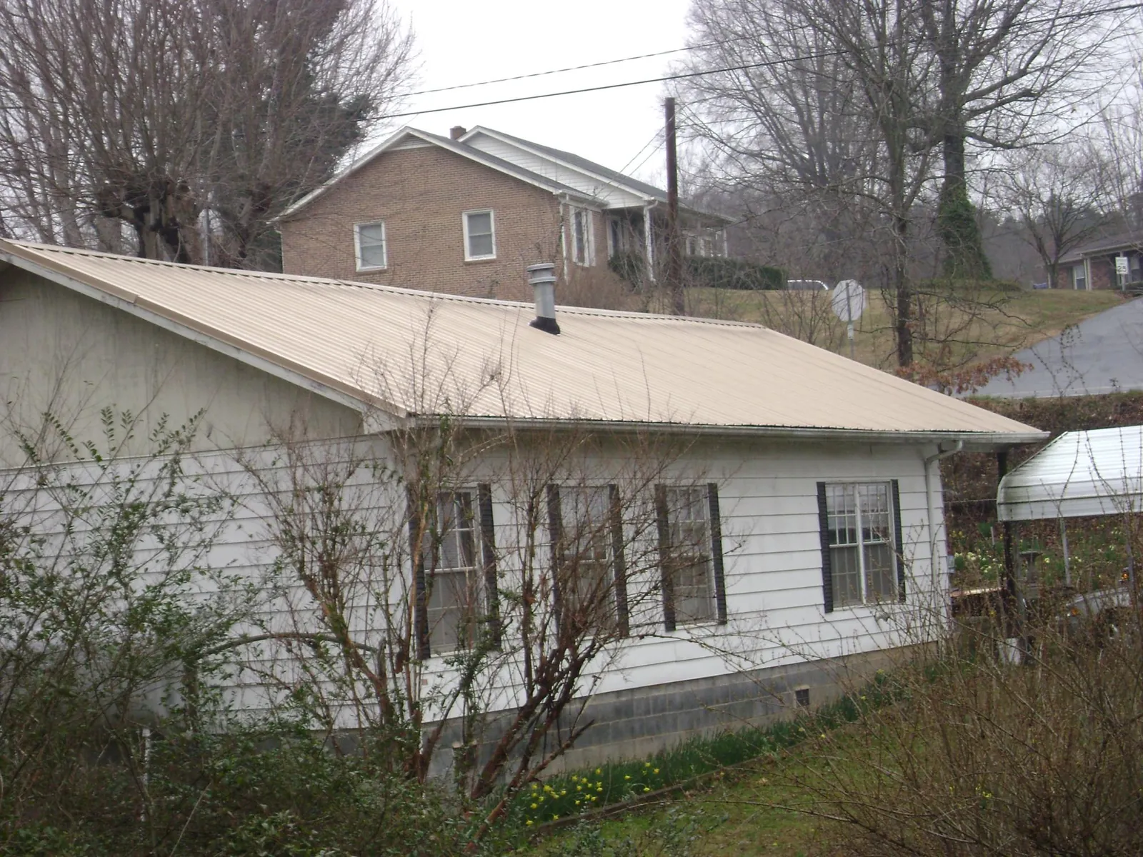Tan metal roof on a white sided house set into a hillside — Commercial Roofing by Roofing Brothers in Upsala
