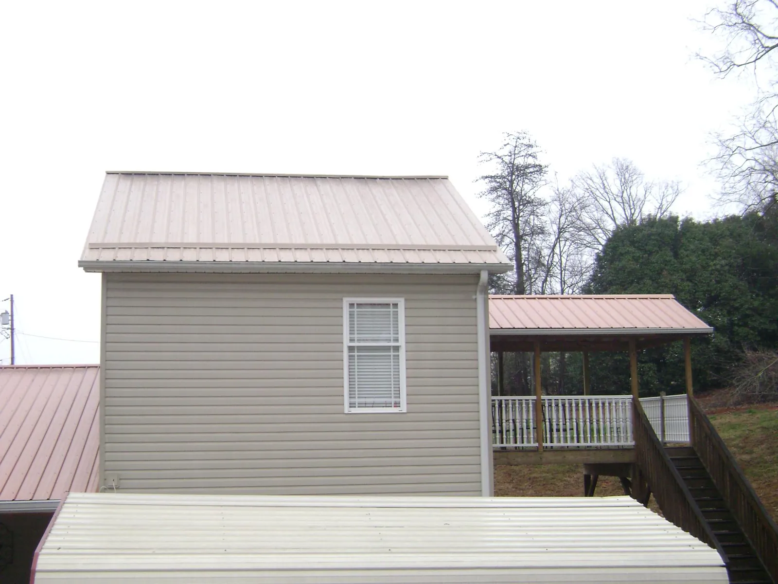 Tan metal roofs on a two story addition and attached porch, from a Roof Replacement job in Upsala